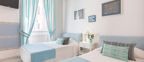 A bedroom with two beds, a nightstand, a potted plant, and a wall-mounted TV.
