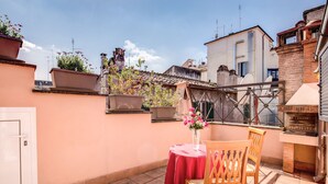 A terrace with a table and chairs, potted plants, and a brick oven. - Pantheon Rooms (Rome)