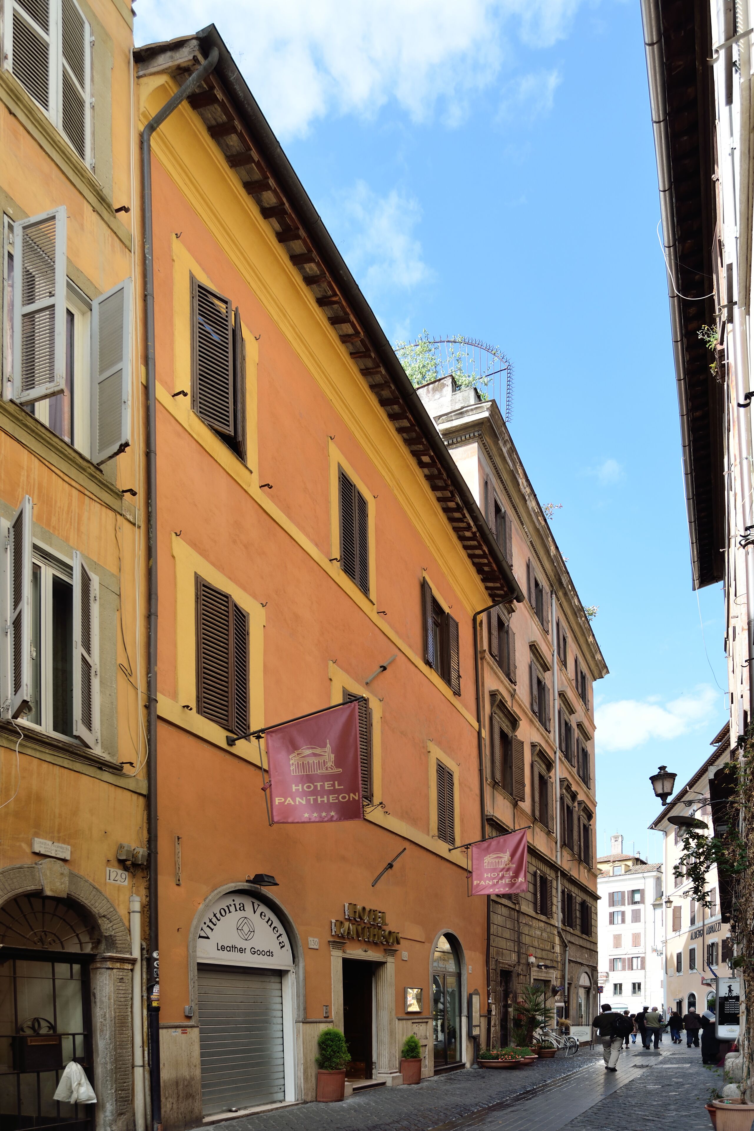 Una calle estrecha con edificios que presentan puertas arqueadas y contraventanas. Se ve un cartel de "Hotel Pantheon".