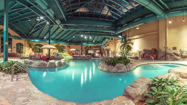 Une piscine intérieure agrémentée d’un décor rocheux, de chaises longues et d’une cascade.