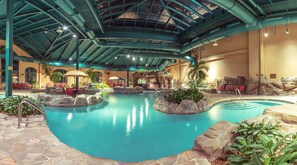 An indoor pool with a rocky landscape, lounge chairs, and a waterfall feature. - Paragon Casino Resort (Marksville)