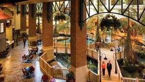 Un vaste atrium à plusieurs niveaux, agrémenté d’un élément aquatique central, de rampes en bois et de plantes suspendues.