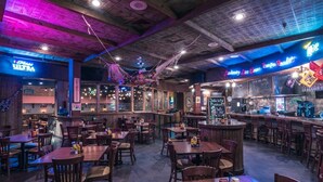 Un restaurant avec des tables et des chaises en bois, un coin bar et des enseignes au néon.