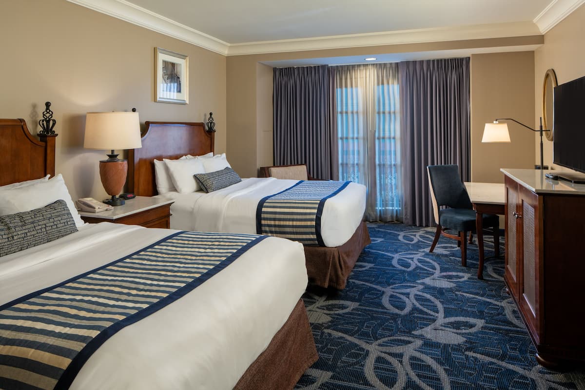 A hotel room with two beds, a desk, a chair, and a TV.