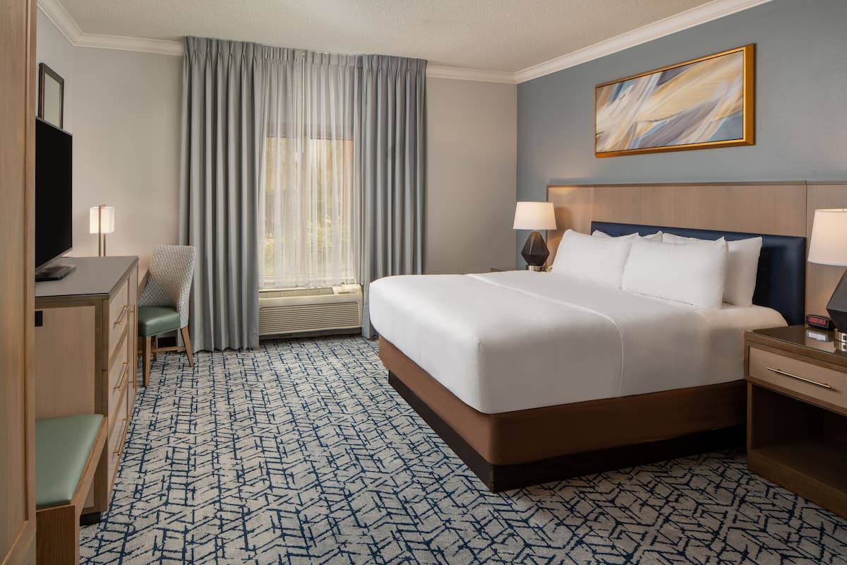 A hotel room with a large bed, a desk with a chair, a TV, and a window with curtains.