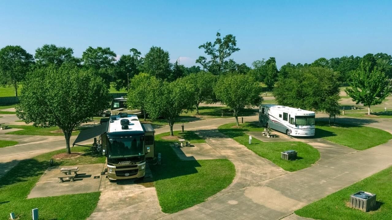 A campground with RVs parked on a paved area surrounded by trees and grass.
