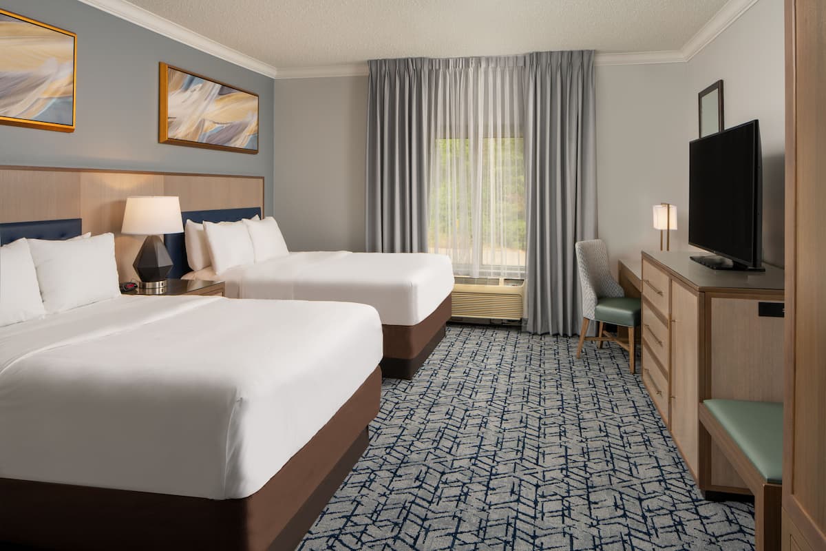 A hotel room with two beds, a desk, a television, and a window with curtains.