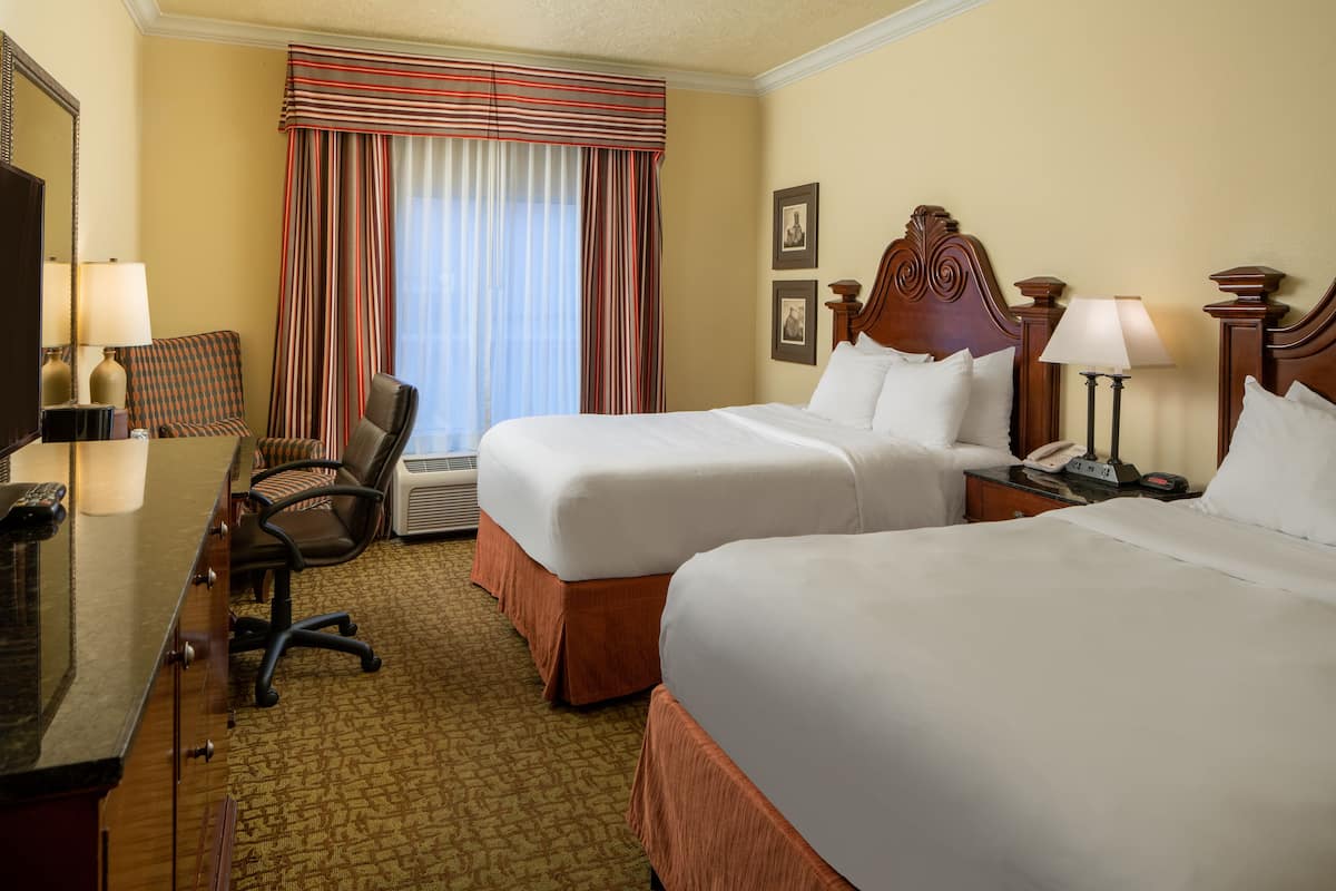 A hotel room with two beds, a desk with a computer, a chair, a desk lamp, and a telephone.
