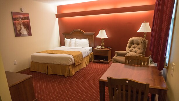 A hotel room with a bed, bedside table, lamp, chair, and a small table.