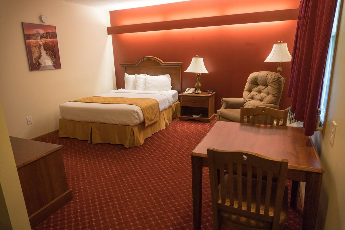 A hotel room with a bed, bedside table, lamp, chair, and a small table.
