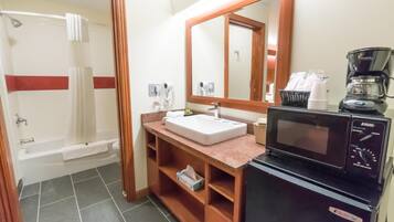 A bathroom with a bathtub, a sink, a mirror, a microwave, and a coffee maker.