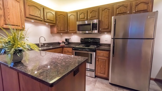 Una cocina con armarios de madera, un refrigerador de acero inoxidable, un microondas, una estufa y una encimera de granito.