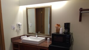 Un baño con un lavabo blanco, un espejo grande, un secador de pelo, una cafetera y un microondas.