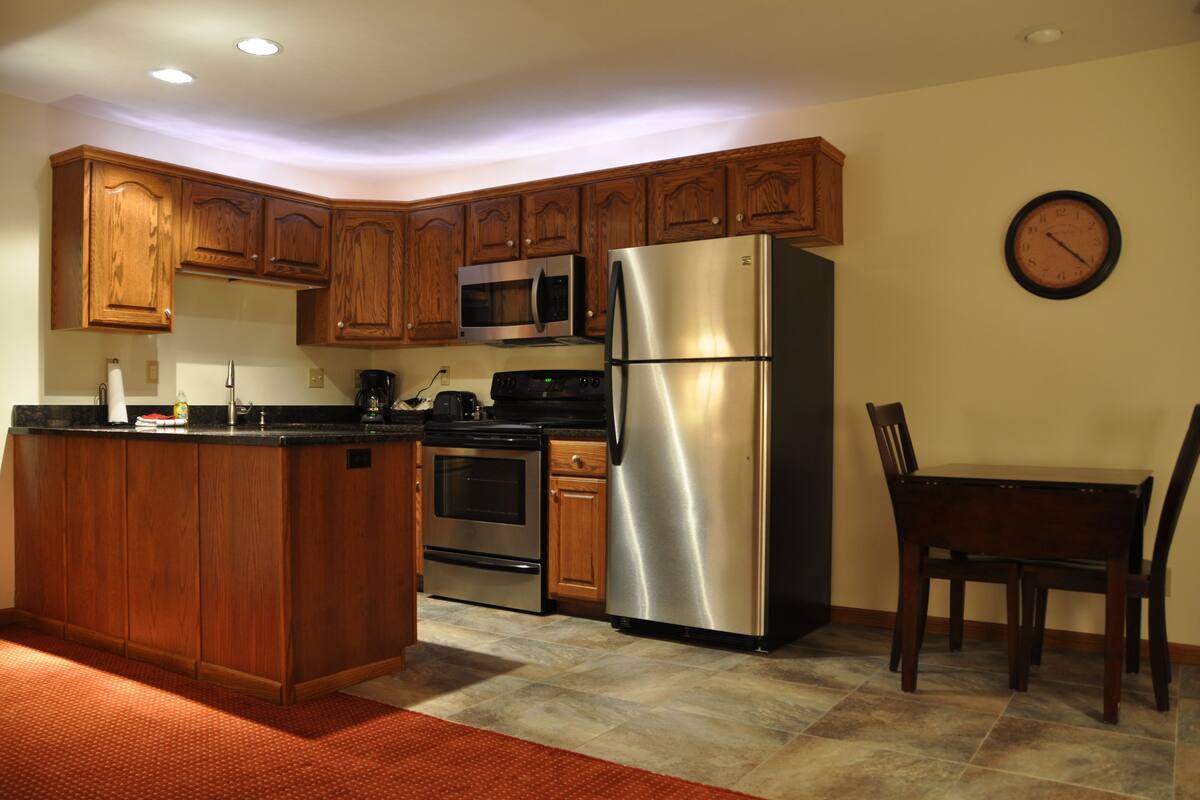A kitchen with wooden cabinets, stainless steel appliances, a microwave, and a clock on the wall.