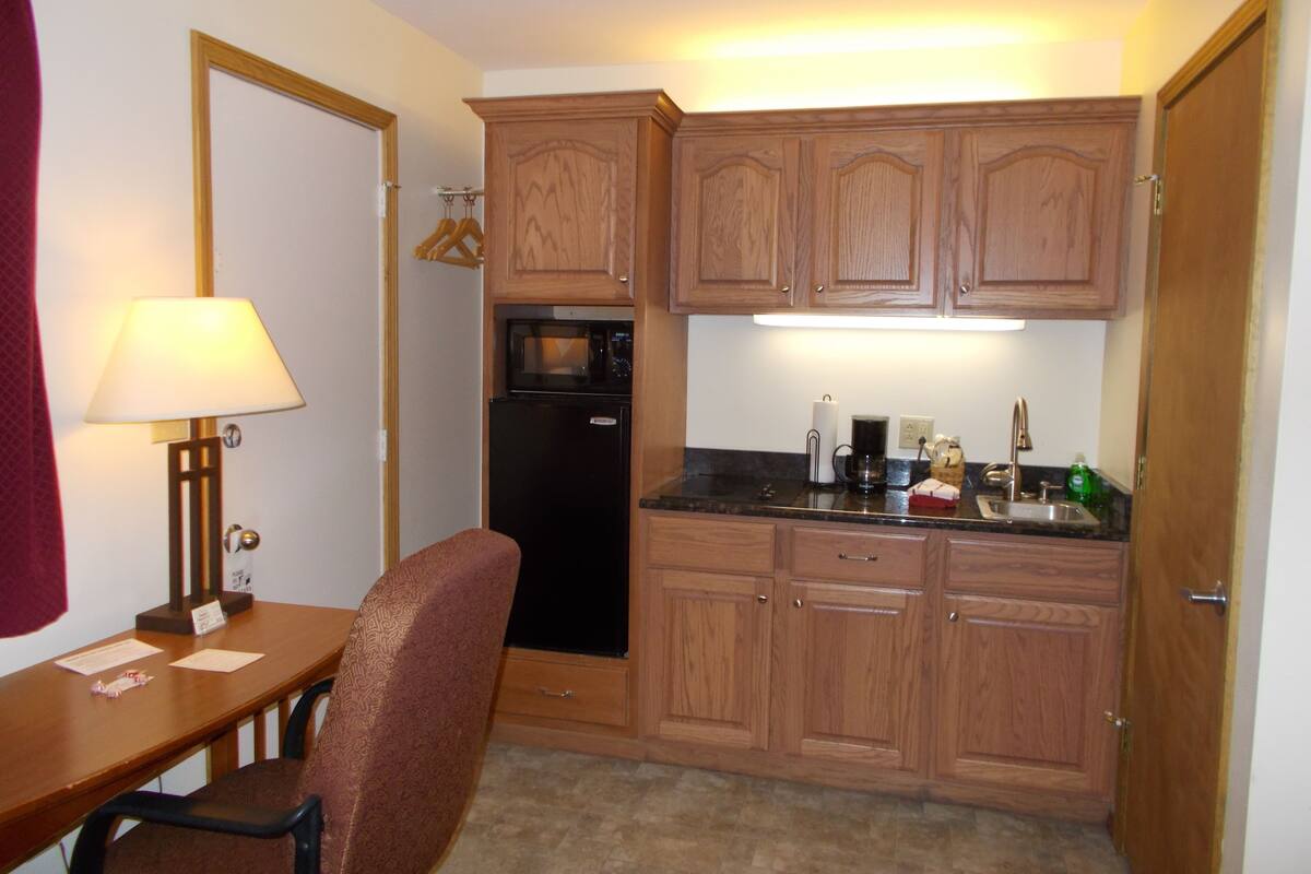 A compact kitchen with wooden cabinets, a refrigerator, a microwave, a coffee maker, and a sink.
