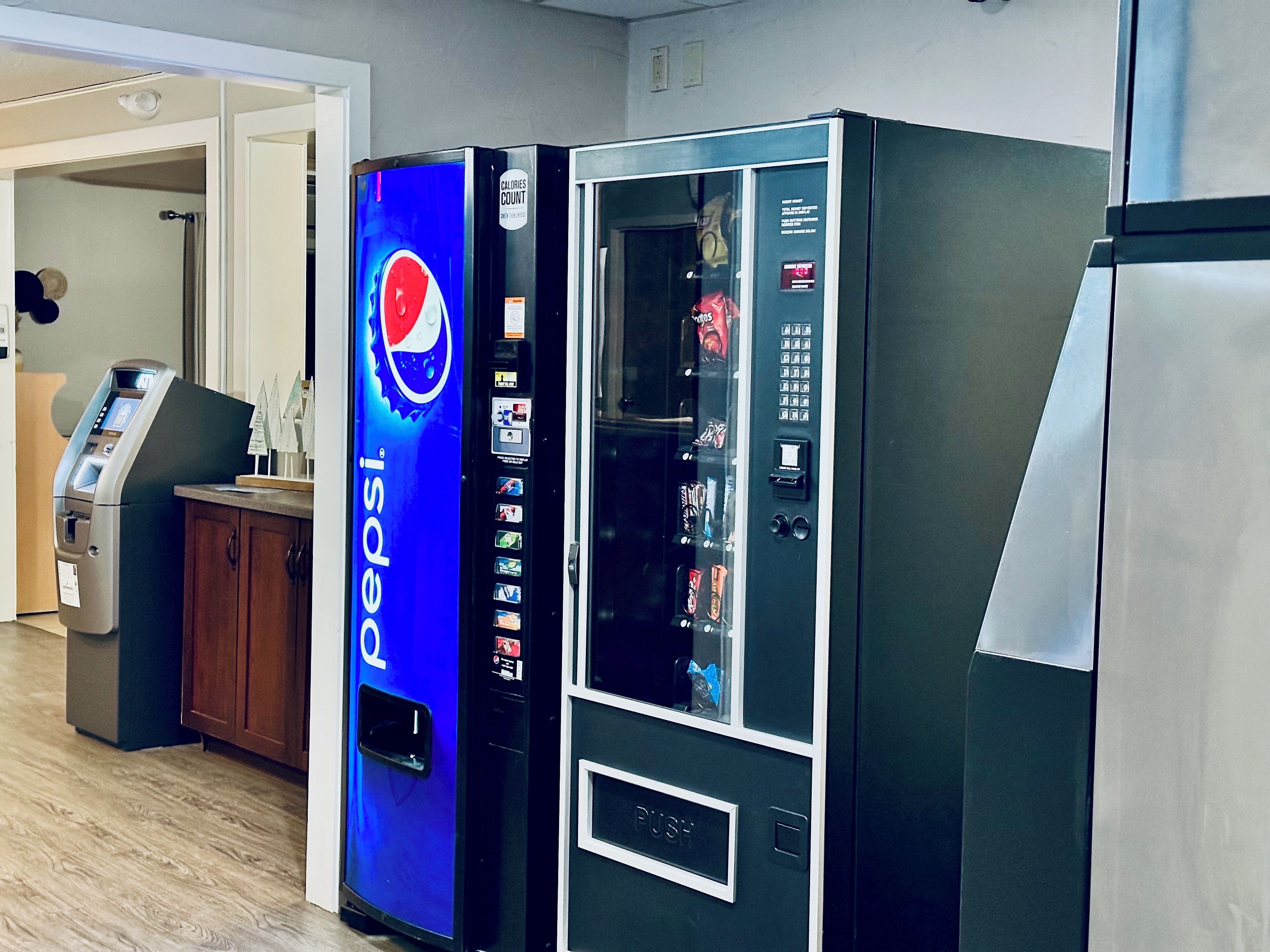 Un espace comprenant un distributeur automatique de boissons de la marque Pepsi et un réfrigérateur.