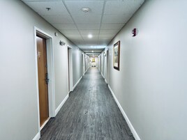 Un pasillo largo y estrecho con puertas de madera a un lado y cuadros enmarcados al otro.
