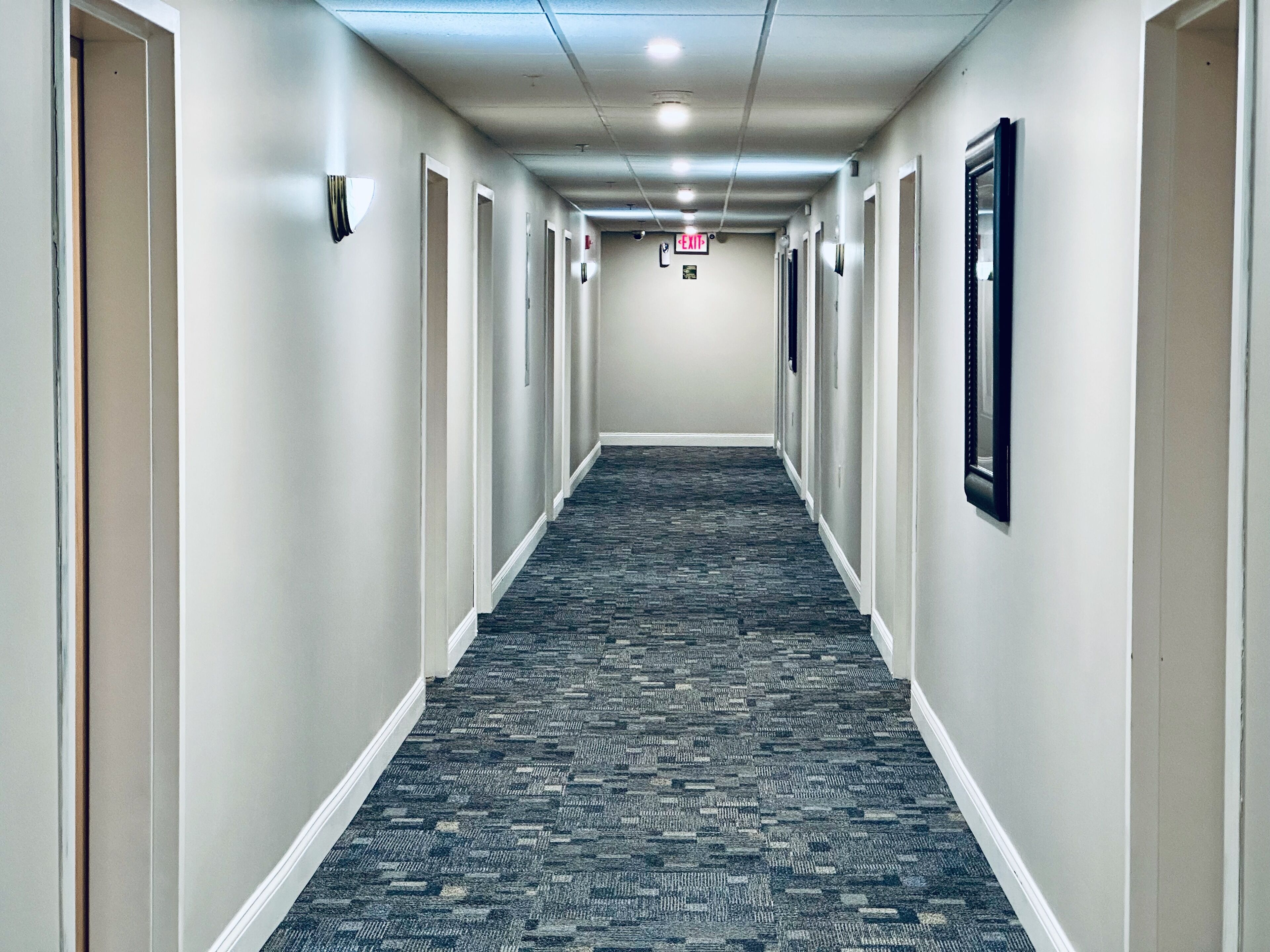 A hotel hallway with carpeted floors, white walls, and doors on both sides.