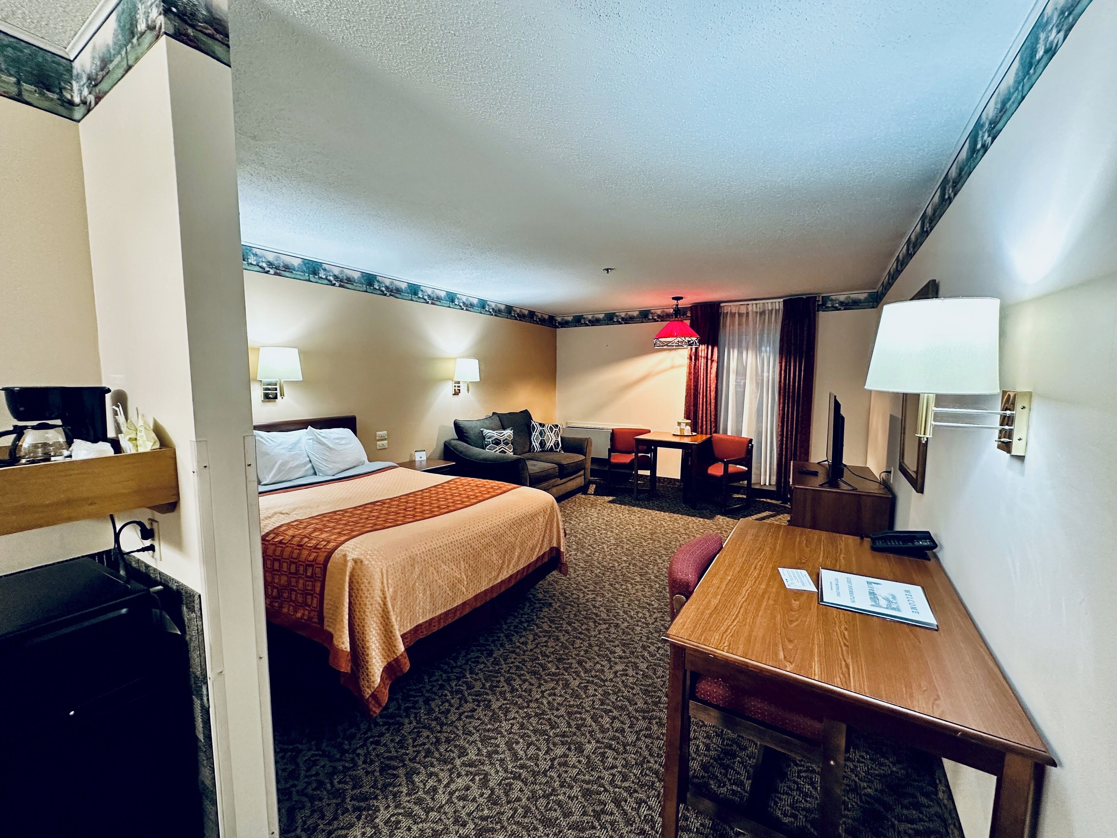 Habitación de hotel con cama, escritorio, silla, mesa, lámpara y televisor.