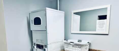 A laundry area with stacked washers and dryers, a basket for laundry, and a sign instructing on detergent use.