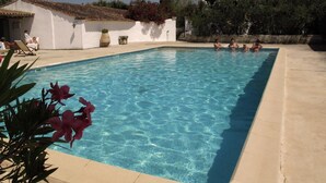 A rectangular swimming pool with clear blue water, surrounded by a beige tiled deck. There are lounge chairs and a white building with a tiled roof in the background. - Cacharel (Saintes-Maries-de-la-Mer)