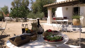 An outdoor dining area with a table set for two, featuring a salad, wine, and bread baskets. - Cacharel (Saintes-Maries-de-la-Mer)