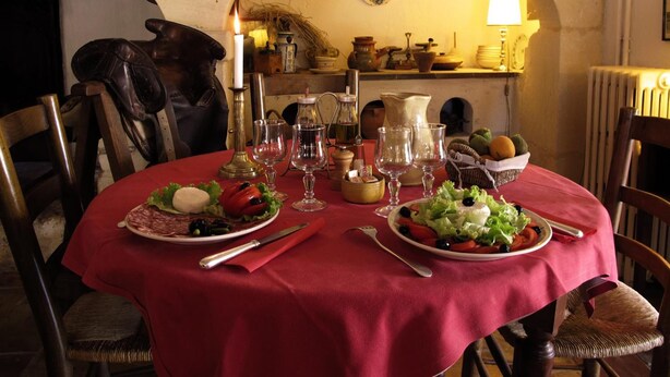 A dining table set with plates of food, glasses, and cutlery, surrounded by chairs in a room with an arched doorway and rustic decor. - Cacharel (Saintes-Maries-de-la-Mer)