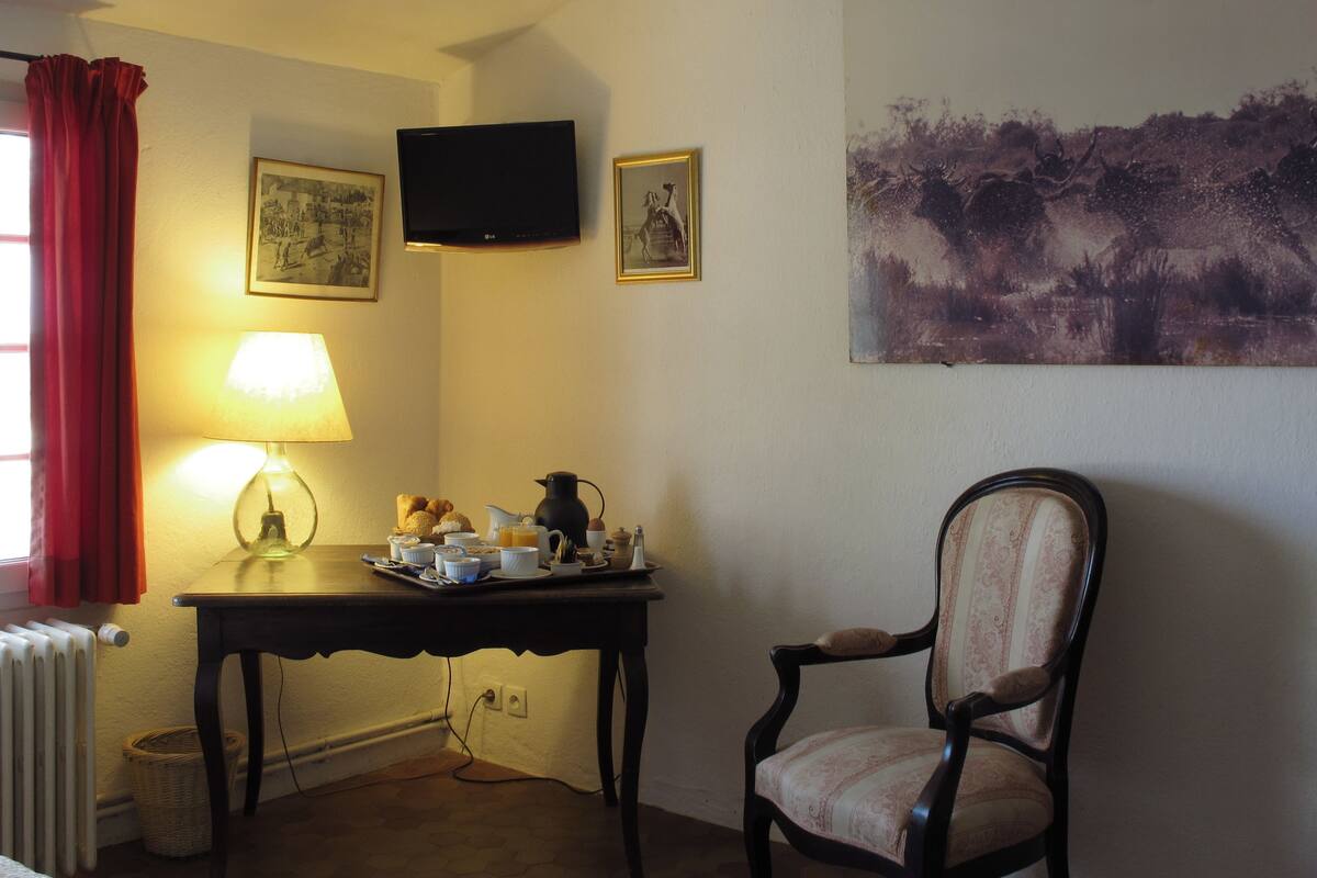 Ein Essbereich mit einem für das Frühstück gedeckten Tisch, einem Stuhl, einem an der Wand montierten Fernseher und einem Gemälde über dem Tisch.