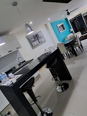 A modern kitchen with a black countertop, bar stools, and a dining area with a white sofa and a blue accent wall. - Capital St. (Mexico City)