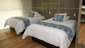 A hotel room with two beds, each with white bedding and striped blankets. The room has wooden flooring and a modern headboard with built-in shelves. - Capital St. (Mexico City)