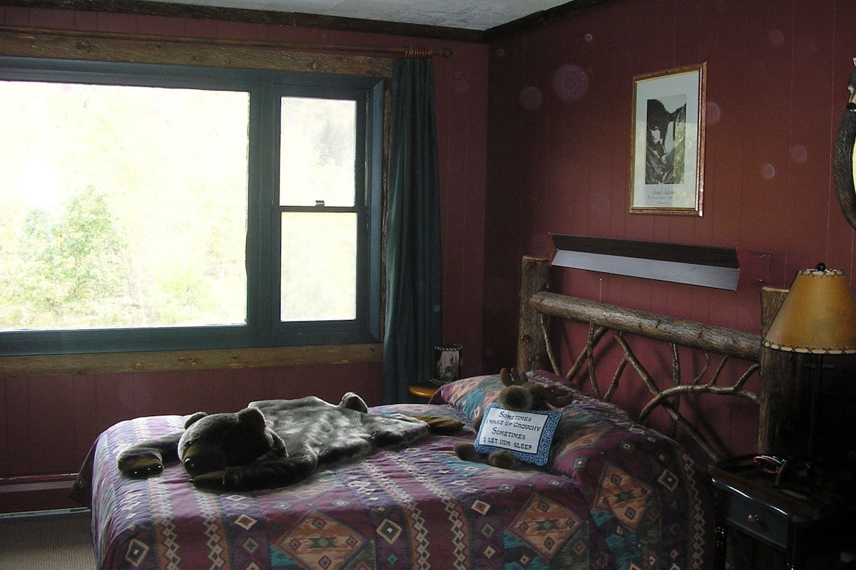 A bedroom with a bed, a window, a lamp, and a framed picture on the wall.