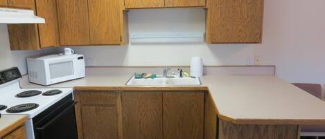 Une cuisine de taille réduite, avec des meubles de rangement en bois, une cuisinière blanche, un four à micro-ondes et un évier.