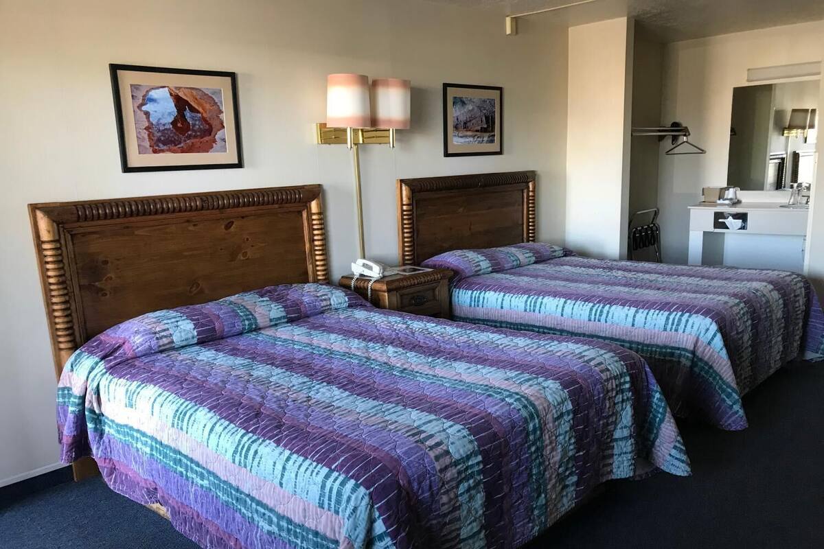 Une chambre d’hôtel avec deux lits, une table de chevet, une lampe et un petit bureau avec un miroir.