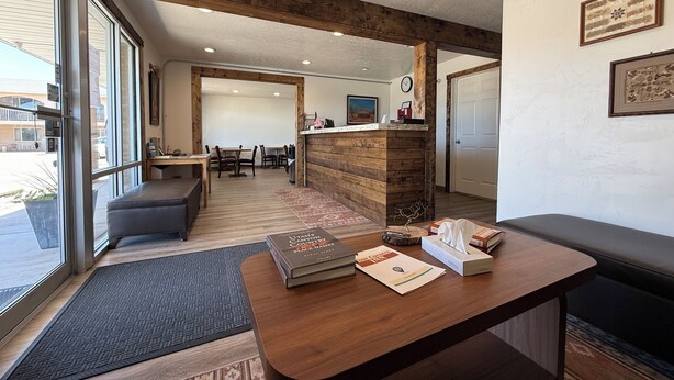 Un comptoir d’accueil en bois, un banc, un tapis et une porte donnant sur un espace repas avec des tables et des chaises.