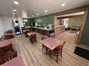 A restaurant with wooden tables and chairs, a counter with a coffee machine, and a trash bin.