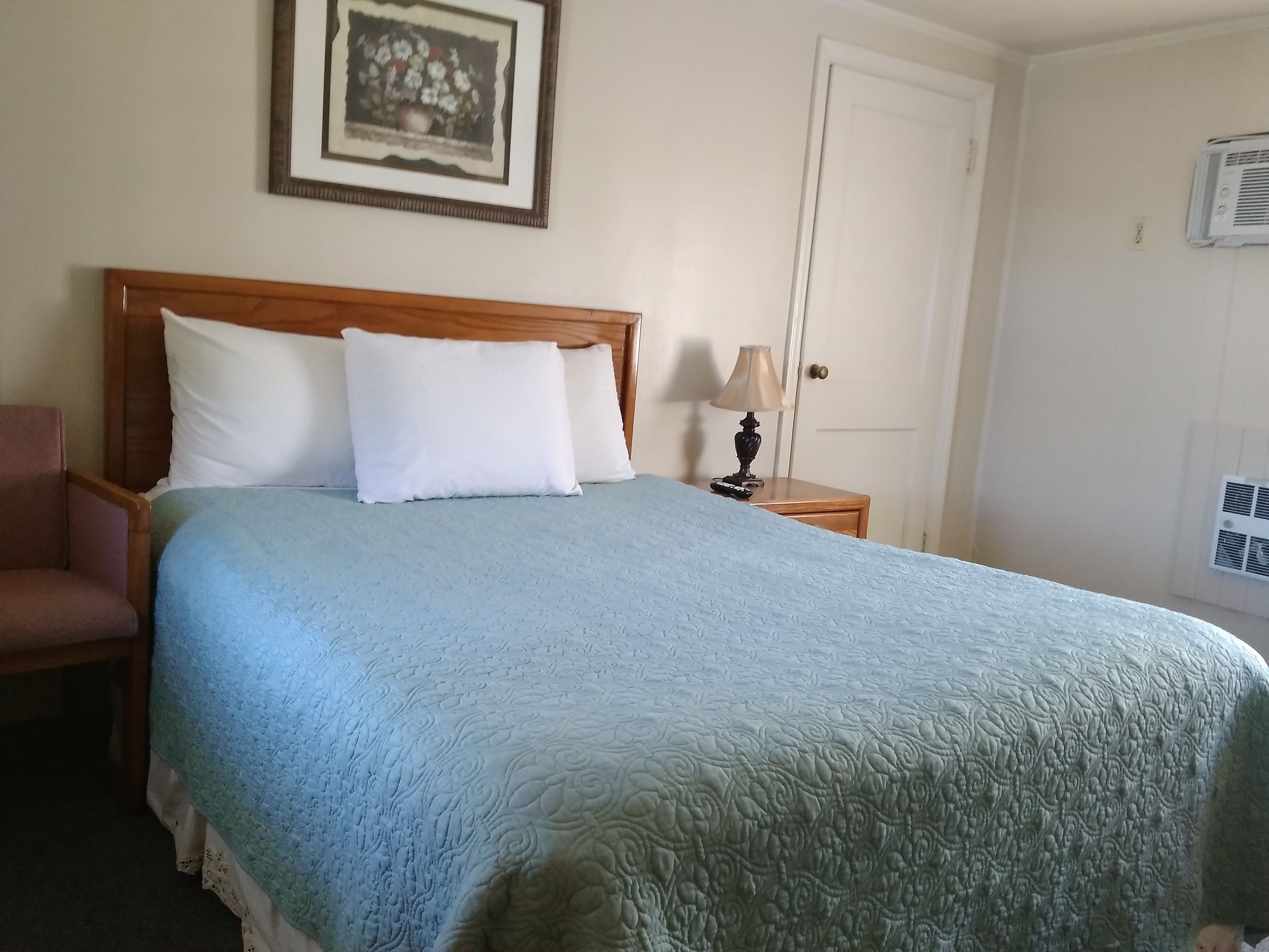 A neatly made bed with a blue quilt, a wooden headboard, and a white pillow.