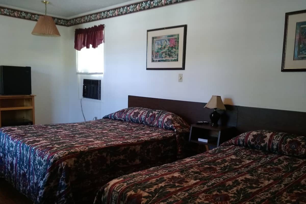 Quarto de hotel com duas camas, televisão, abajur e um quadro na parede.