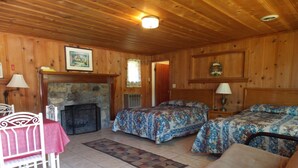 A cozy cabin-style room with a fireplace, two beds with floral bedding, a dining table with a red tablecloth, and a wooden ceiling. - Clarketon Motel (Maggie Valley)