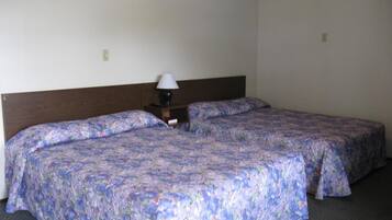 A hotel room with two single beds, a wooden headboard, a nightstand with a lamp, and a floral-patterned bedspread.