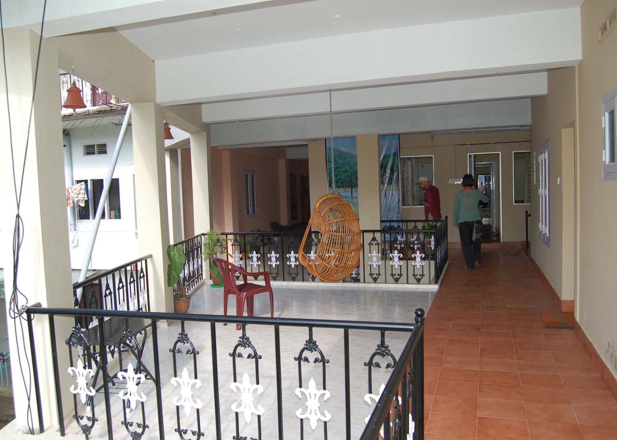 A spacious indoor area with a tiled floor, a balcony with a wicker chair, and a railing with decorative elements.