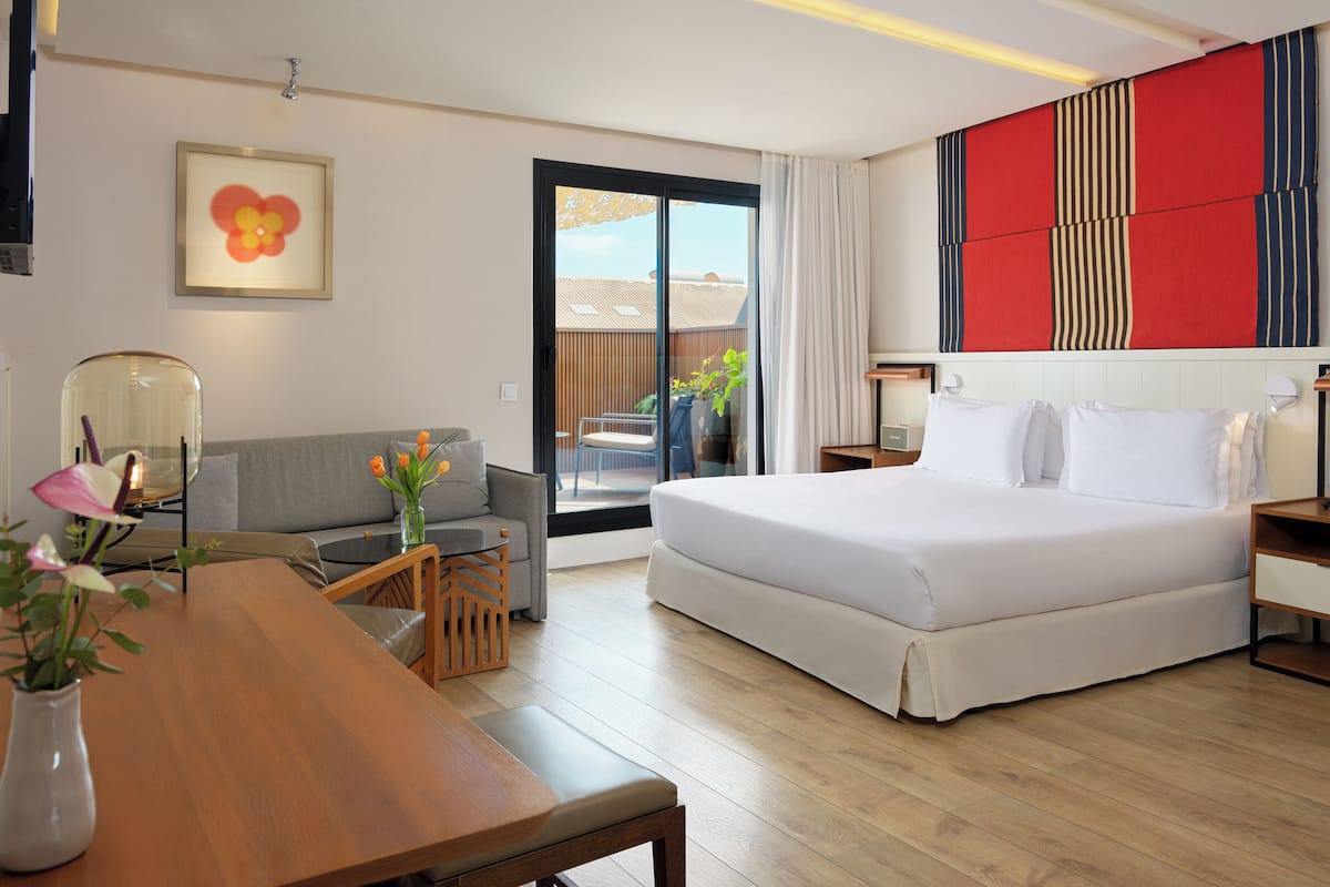 Ein modernes Hotelzimmer mit einem großen Bett, einer Couch, einem Esstisch und Blick ins Freie.
