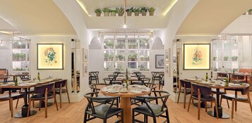 Un comedor moderno con varias mesas y sillas, ventanas amplias con persianas y obras de arte enmarcadas en las paredes.