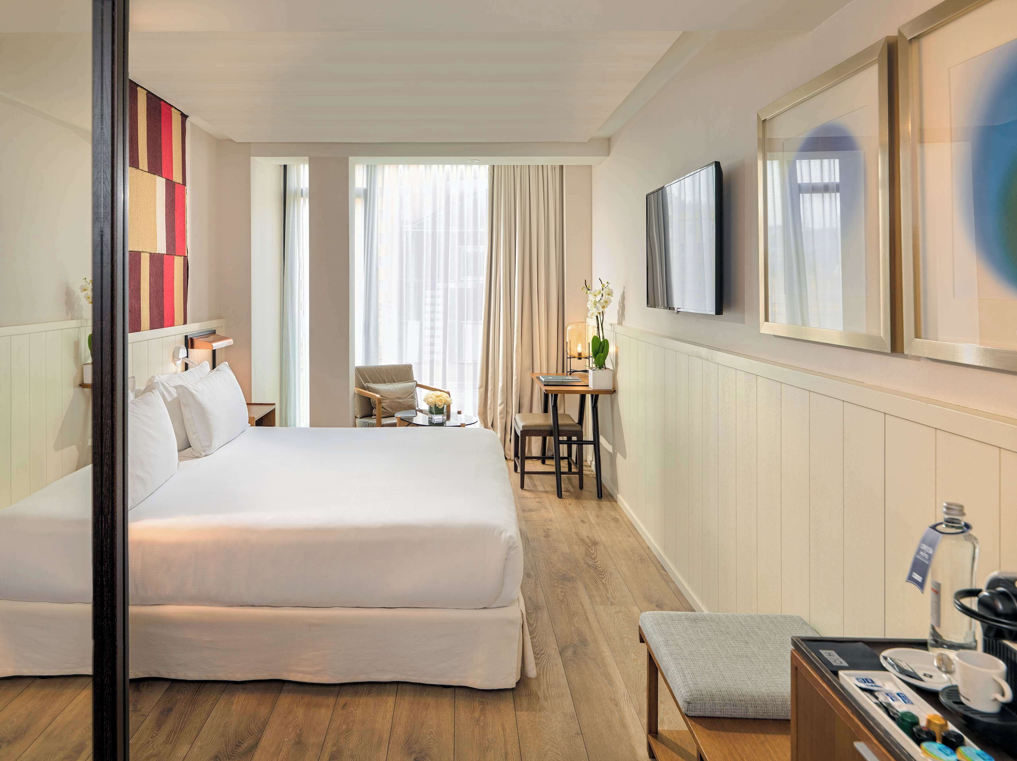 Una habitación de hotel con una cama grande, un escritorio con silla, televisión y ventana con cortinas.