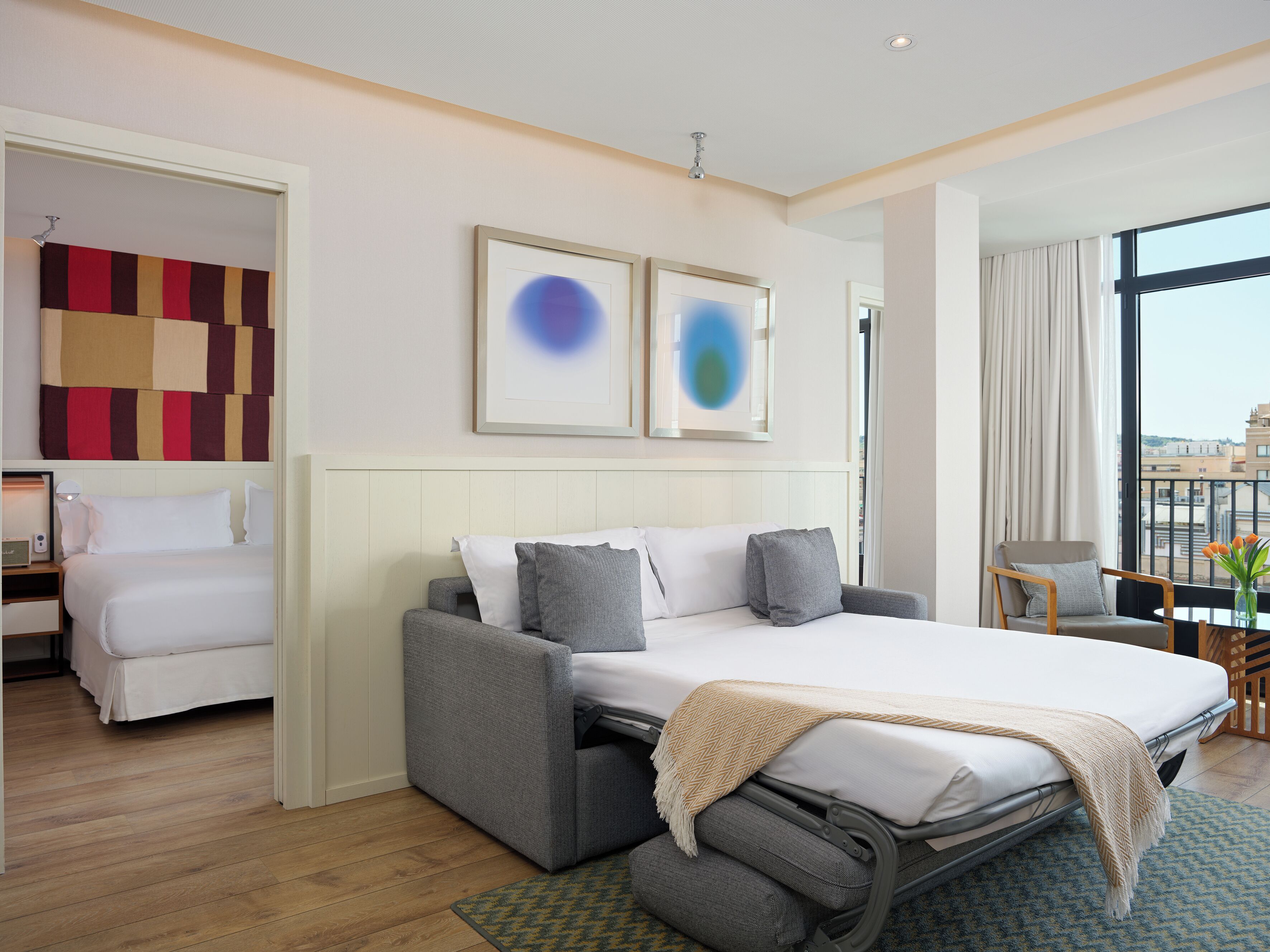 Habitación de hotel con cama, sofá, escritorio y vistas a la ciudad.