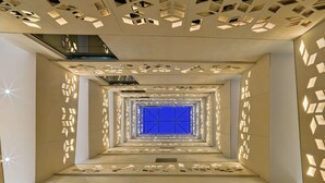 Un interior moderno con patrones geométricos en paredes y techo, una ventana central iluminada en azul y un diseño limpio y minimalista.