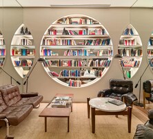 A modern library with a central circular bookshelf surrounded by leather sofas and a coffee table.