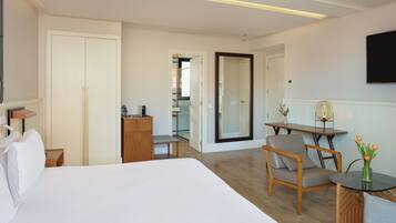 Una habitación de hotel con una cama grande, un escritorio con una silla, una mesita con un jarrón de flores, un armario y un espejo.
