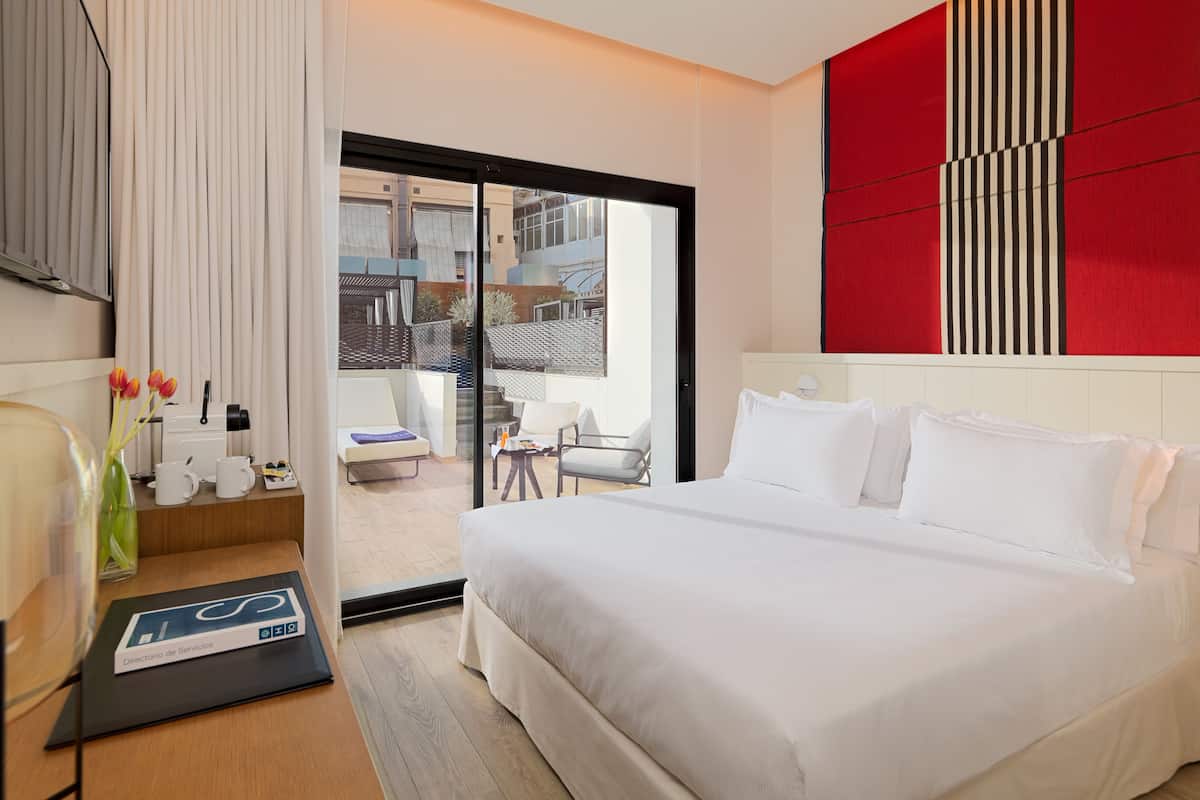 Ein Hotelzimmer mit einem großen Bett, einem Schreibtisch mit Computer, einem Sessel und Blick auf den Balkon.