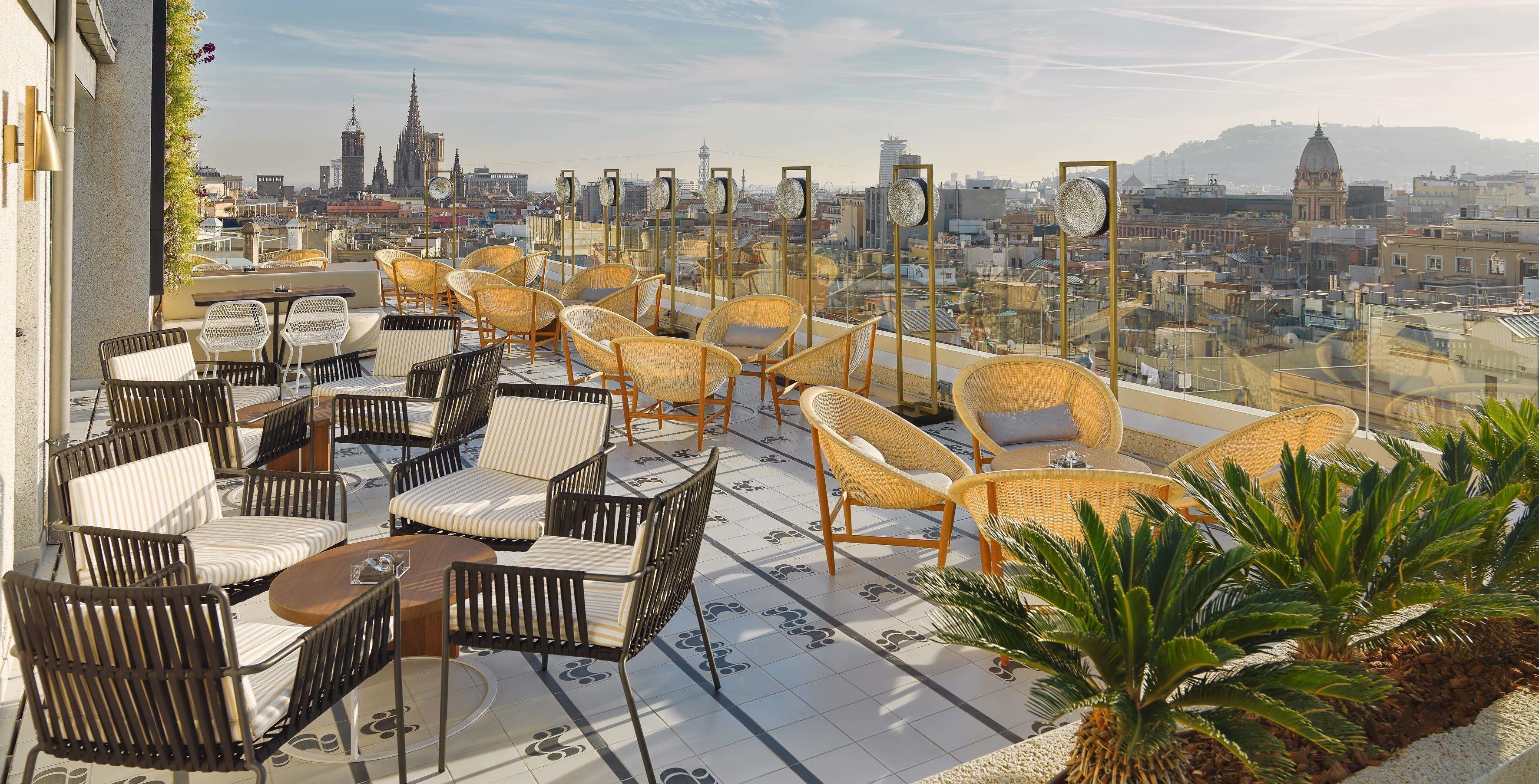A rooftop terrace with wicker chairs and tables, offering a city view.