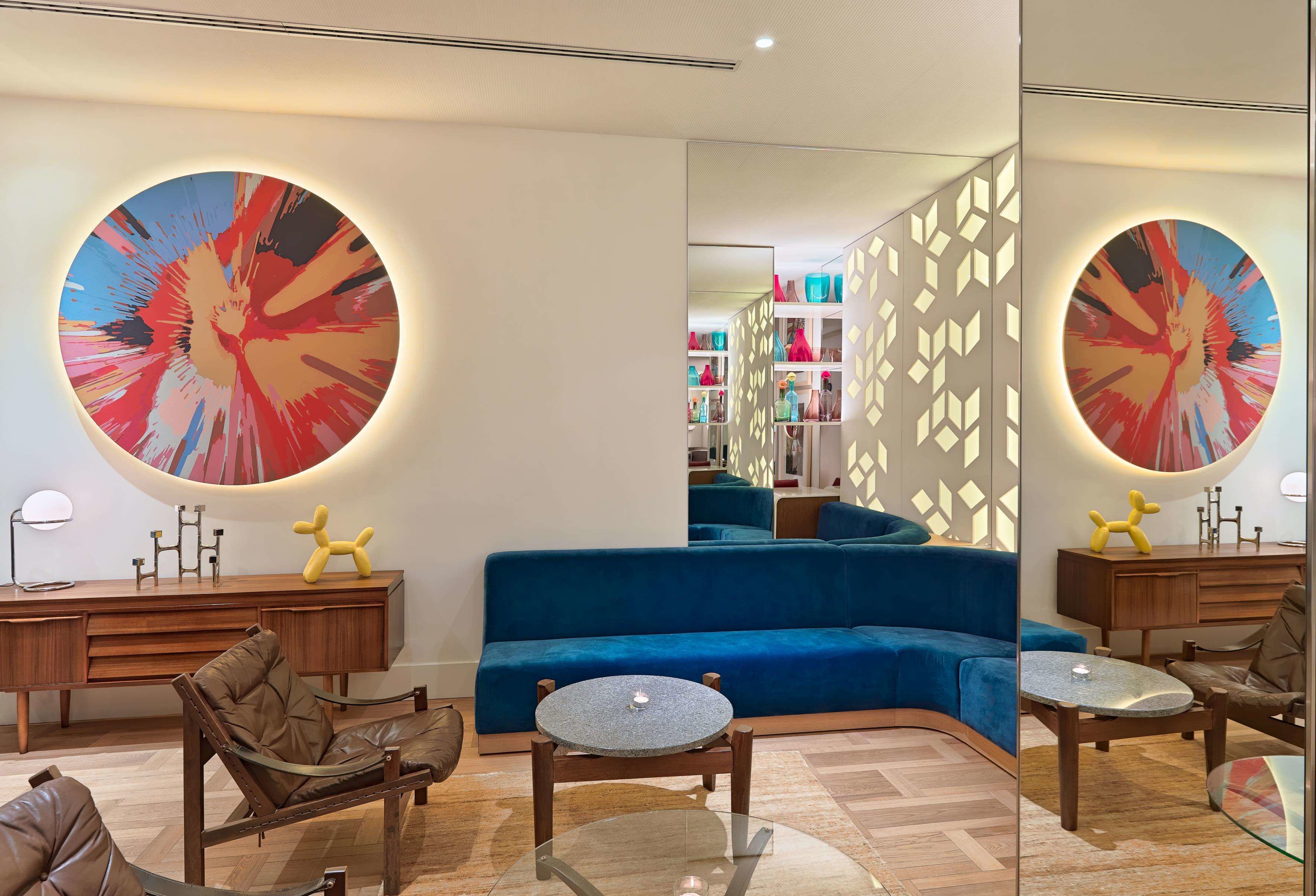A modern living room with a blue sofa, leather armchairs, a glass coffee table, and a wooden sideboard.
